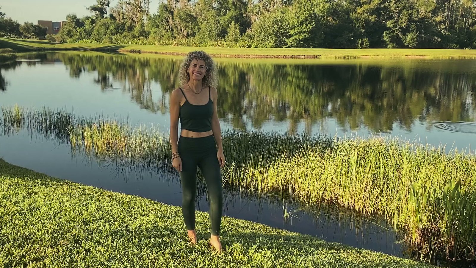 Ana, de pie junto a un lago al sol de la tarde, sonríe a cámara