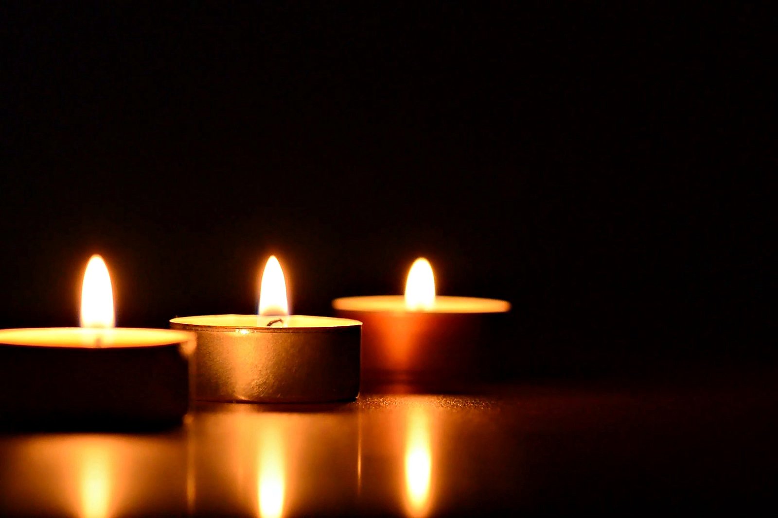 Tres velas pequeñas encendidas sobre una superficie oscura, con la llama quieta